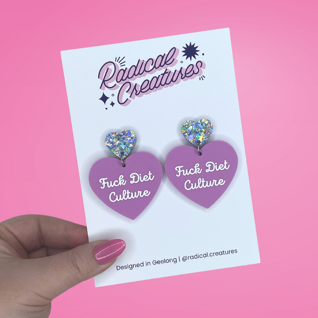 Pastel heart shaped earrings with sparkly heart shaped earring topper. Pastel purple/mauve with words Fuck Diet Culture in white.