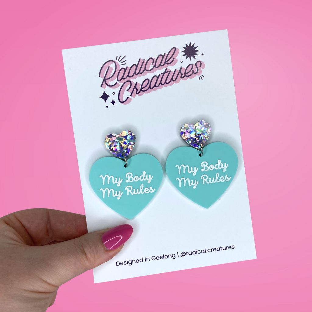 Pastel heart shaped earrings with sparkly heart shaped earring topper. Pastel mint green with words My Body My Rules in white.