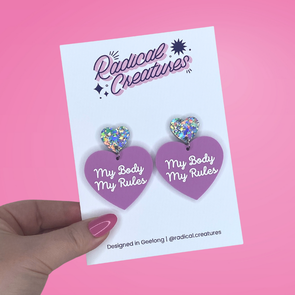 Pastel heart shaped earrings with sparkly heart shaped earring topper. Pastel purple/mauve with words My Body My Rules in white.