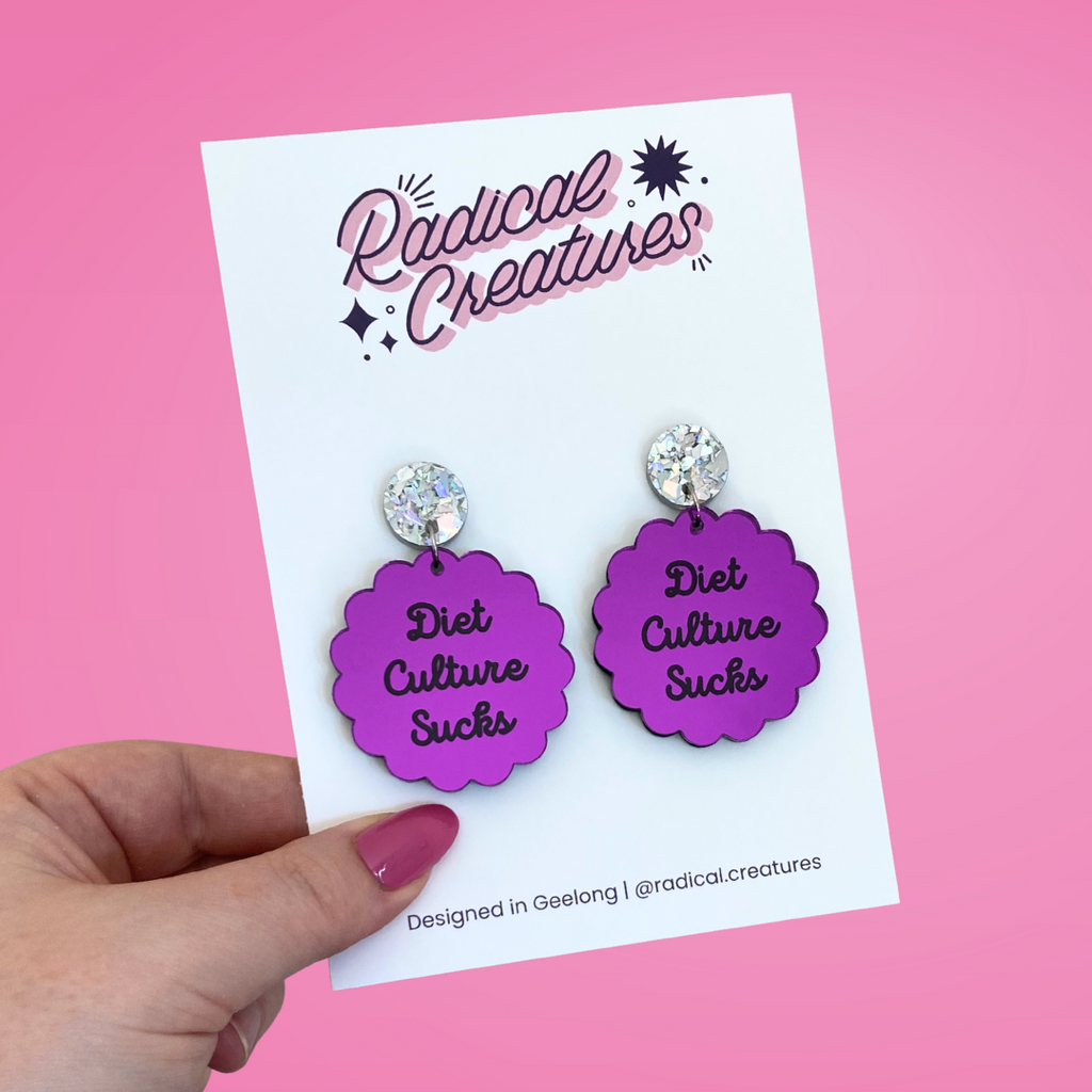 Scalloped circle shaped dangle earrings with sparkly earring topper. Purple mirror with text "diet culture sucks"