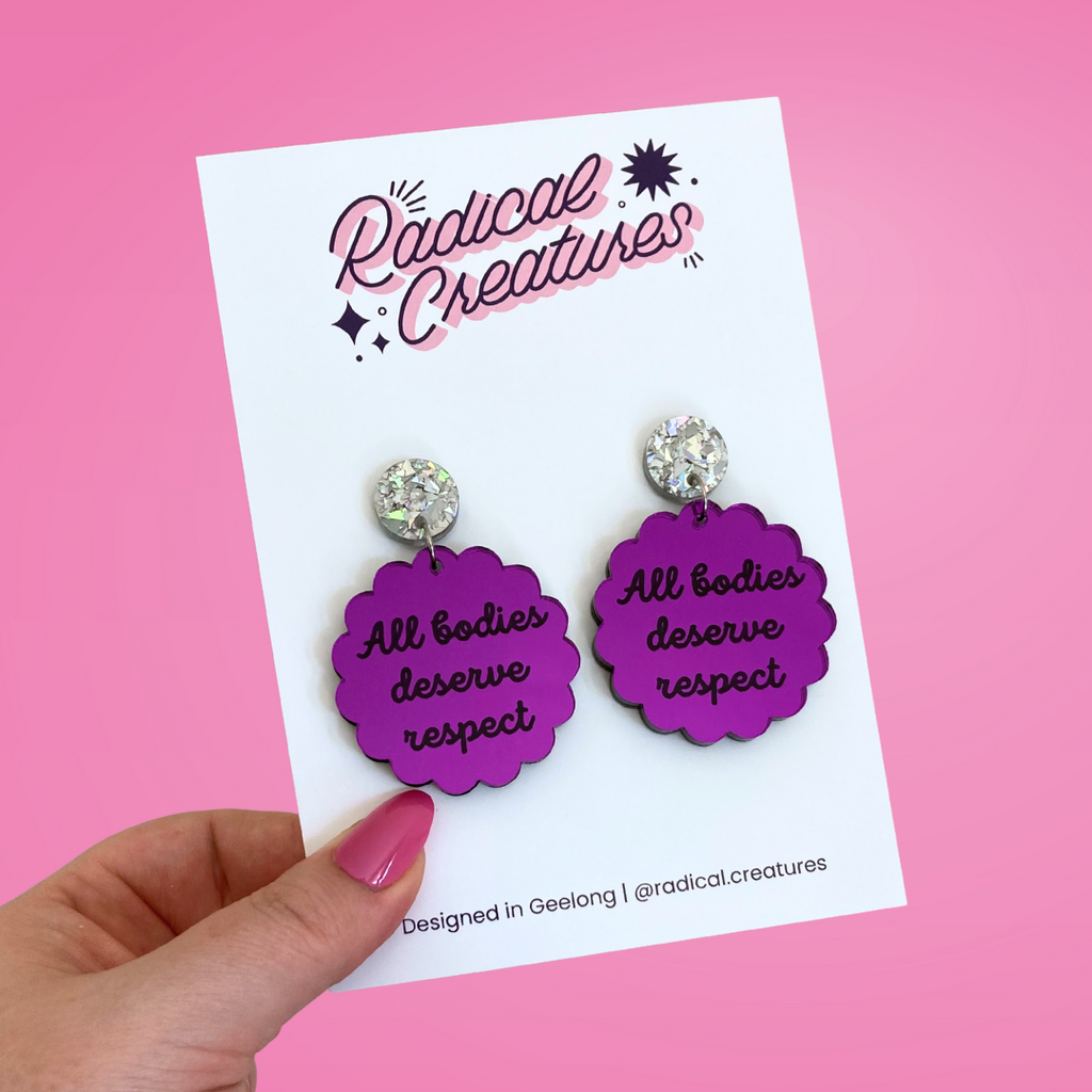 Scalloped circle shaped dangle earrings with sparkly earring topper. Purple mirror with text "all bodies deserve respect"