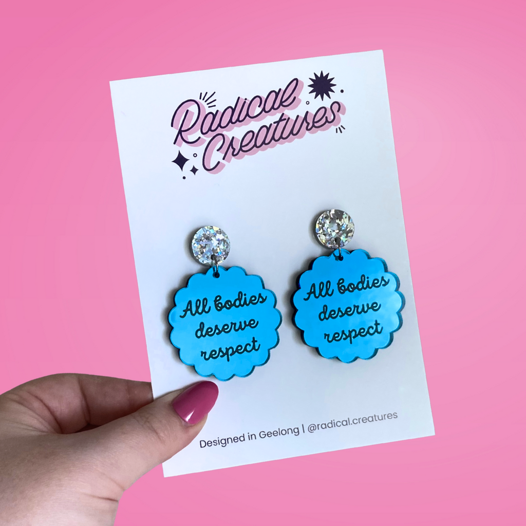 Scalloped circle shaped dangle earrings with sparkly earring topper. Blue mirror with text "all bodies deserve respect"