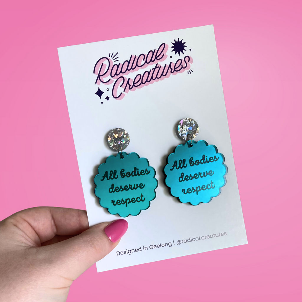 Scalloped circle shaped dangle earrings with sparkly earring topper. Teal mirror with text "all bodies deserve respect"