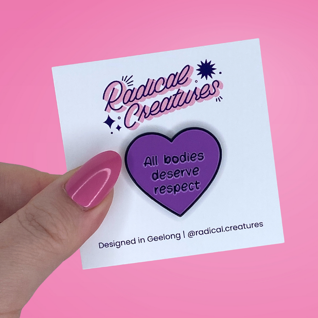 Heart shaped pin. Purple with text "all bodies deserve respect"