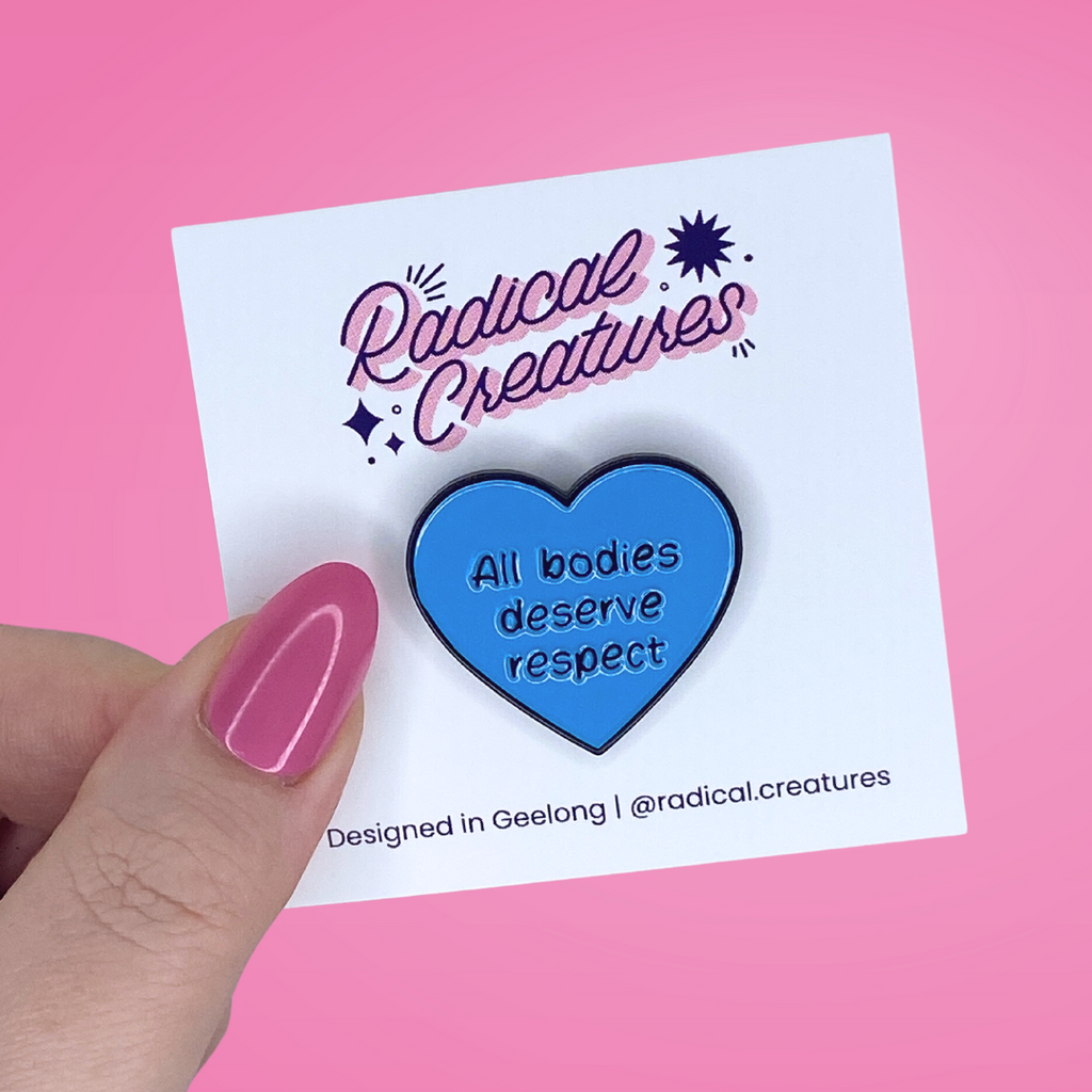 Heart shaped pin. Blue with text "all bodies deserve respect"