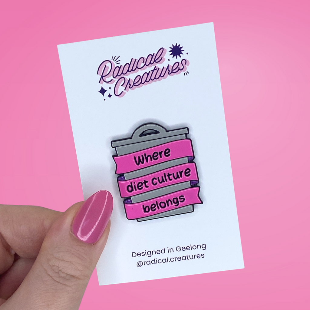 Enamel pin in shape of grey bin, with pink banner wrapped around it that says where diet culture belongs
