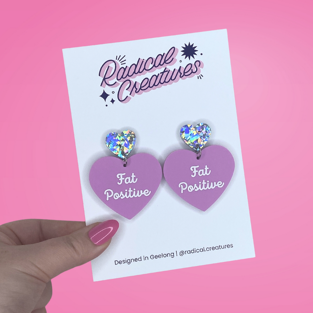 Pastel heart shaped earrings with sparkly heart shaped earring topper. Pastel purple/mauve with words Fat Positive in white.