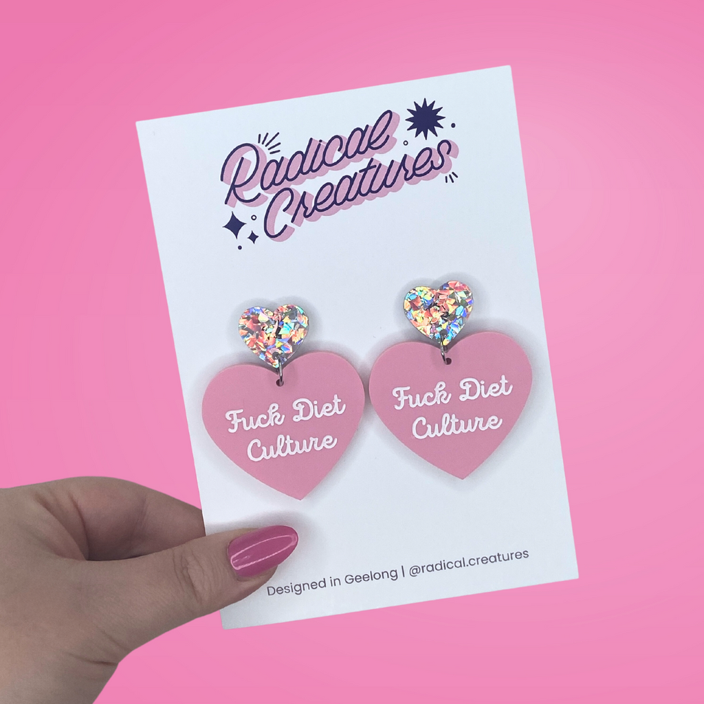 Pastel heart shaped earrings with sparkly heart shaped earring topper. Pastel pink with words Fuck Diet Culture in white.