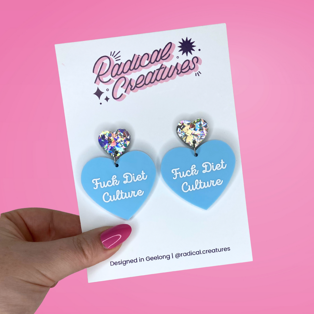 Pastel heart shaped earrings with sparkly heart shaped earring topper. Pastel blue with words Fuck Diet Culture in white.
